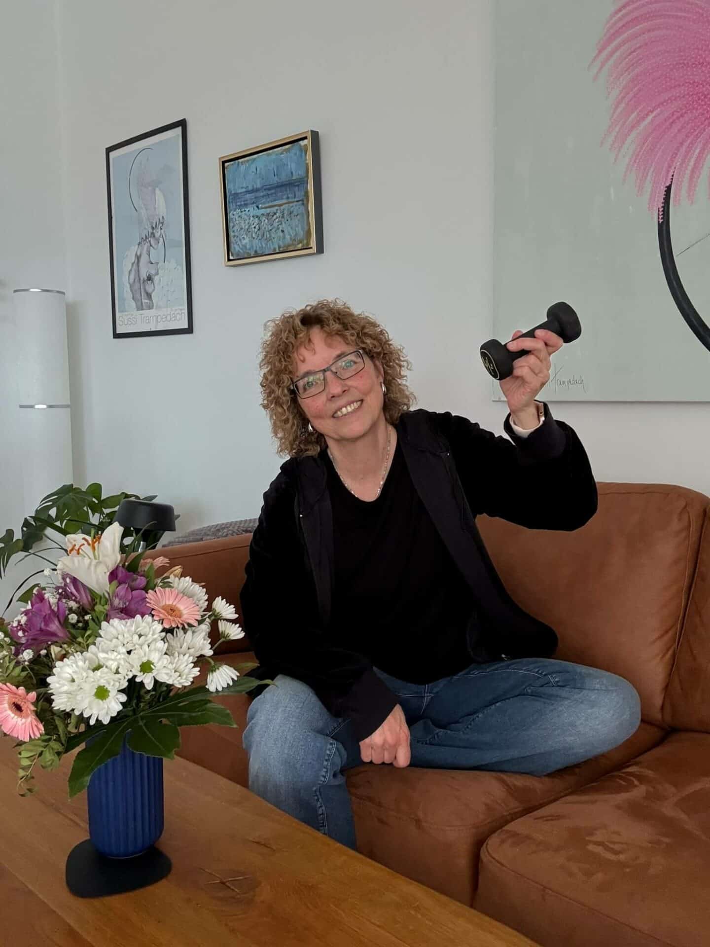 Kvinde i sort trøje sidder i en cognacfarvet sofa med en håndvægt i den ene hånd